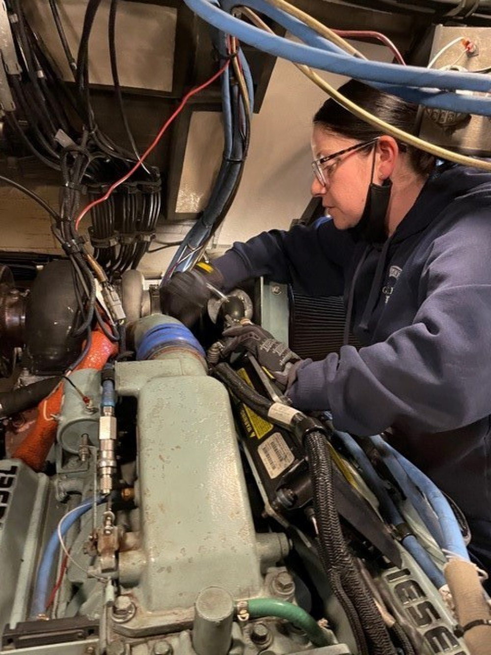 MKC Holly Beck adjusts a hose that connects the air shutdown housing to the turbo on a 6V92TA Detroit Diesel engine (U.S. Coast Guard Photo).