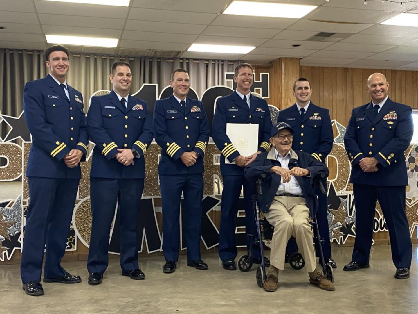 Members from Coast Guard Sector/Air Station Corpus Christi attend a birthday celebration for Michael J. Swierc, Coast Guard veteran who turned 100 years old, Nov. 6, 2021, in Falls City, Texas. Swierc was presented with a hand written letter from the Commandant, as well as a Coast Guard ensign signed by members of Sector/Air Station Corpus Christi and a unit ball cover. (U.S. Coast Guard photo, courtesy Sector/Air Station Corpus Christi)