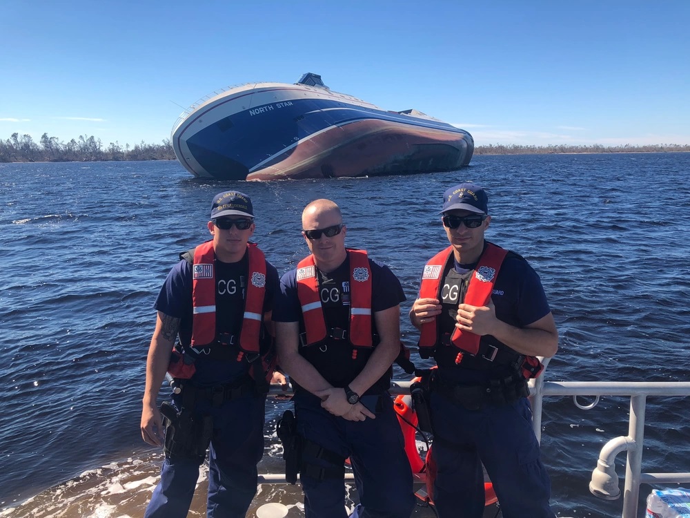 Coast Guard Fort Lauderdale 45-foot Response Boat-Medium crewmembers stand in front of a capsized boat at St. Andrews Bay, Florida, Oct. 22, 2018. The boatcrew spotted the capsized boat during a law enforcement patrol through a Hurricane Michael high-impact area. Coast Guard Photo by Petty Officer 3rd Class David Brindley.