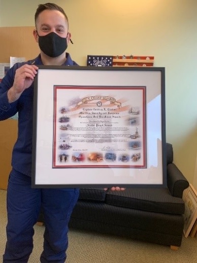Ensign Kirk M. Eastman from Sector Puget Sound, Enforcement Division holding the framed Maritime Security and Response Operations Excellence Award in February 2021. 
