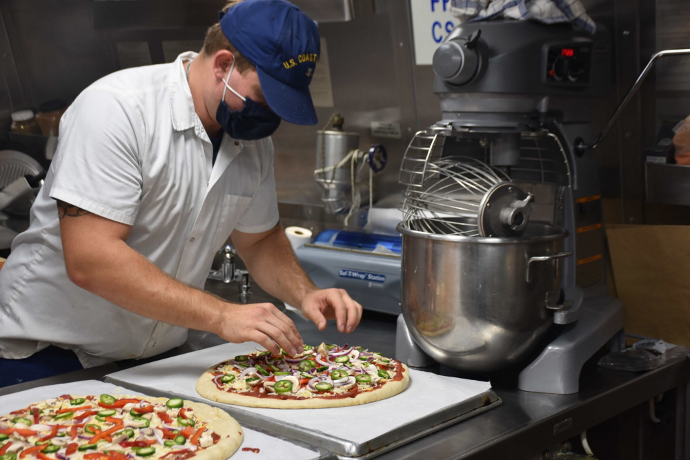 Petty Officer 3rd Class David Coleman, a culinary specialist aboard the Coast Guard Cutter Midgett (WMSL 757), prepares a pizza in the ship's galley, April 10, 2021. Culinary specialists serve aboard Coast Guard cutters and at shore units, and receive training in all aspects of food preparation including culinary fundamentals, advanced culinary methods and techniques, and pastry and baking. U.S. Coast Guard photo.