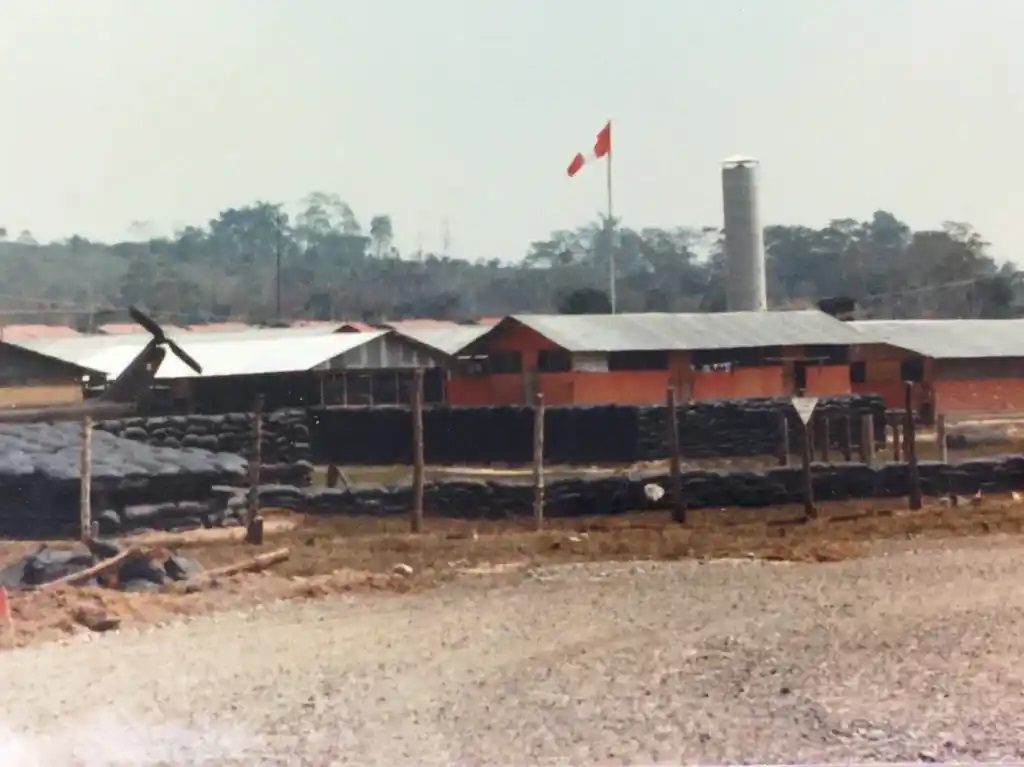 Color photo of Operation Jester’s forward base and airstrip at Santa Lucia, Peru, showing the tail rotor of a Huey helicopter located behind sandbag fortifications. (Coast Guard Aviation Association)