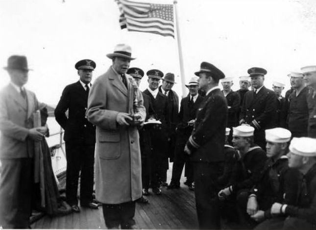 Picture of Lt. Henry Garcia on the fantail of Coast Guard Cutter Shoshone at a formal ceremony receiving the trophy for winning the Coast, Bering Sea Patrol Force rowing competition. Photo shows officers, man and dignitaries from competing cutters and Alaska. (photo by Alan May)
