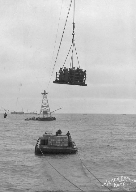 An aerial cable car used to transfer passengers and cargo from ships anchored offshore to the Nome waterfront. Note the tower, which anchored the seaward end of the cable car. Passengers and cargo were loaded onto the car at the base of the tower. Passenger ships anchored offshore are visible in the background. (Library of Congress)