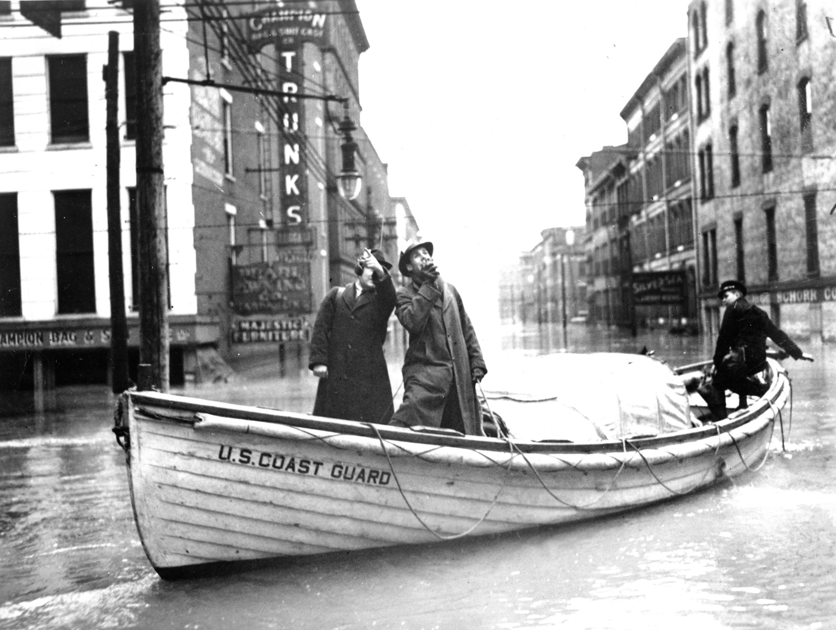 4.	Coast Guardsman motors reporters broadcasting live radio stories of the devastation from flooded city streets in 1937. (U.S. Coast Guard)