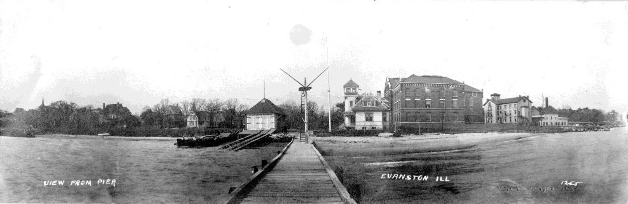 Photograph of entire Station Evanston complex, with the original 1871 boathouse on the left, station wreck pole with dock at center, expanded 1877 station building at right of center, Fisk Hall next to the station, and the remaining structures are NWU buidings. (Photograph courtesy of U.S. Coast Guard Historian’s Office)