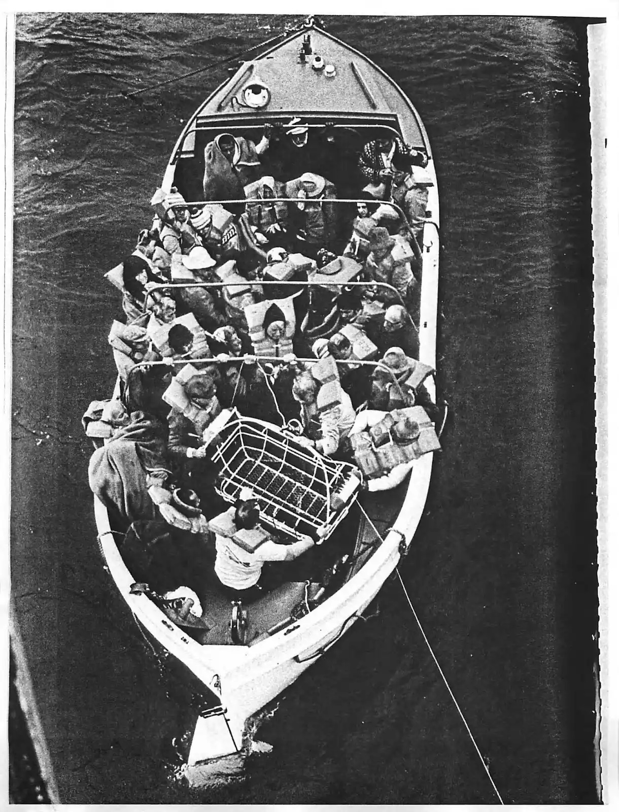 Black and white photo of a Prinsendam motor lifeboat full of passengers during helicopter hoist operations. (Kodiak Maritime Museum)