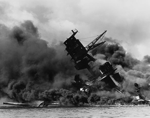 The wreck of the battleship USS Arizona in flames and sitting on the harbor bottom. (National Archives)