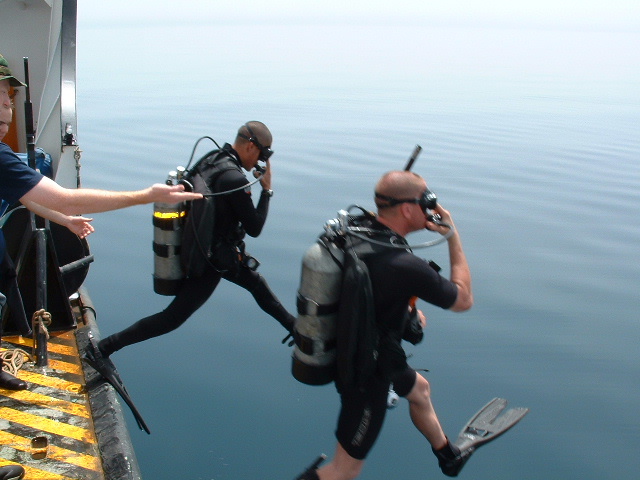 Divers enter the water to survey a buoy in the murky waters of Iraq’s KAA Waterway. (Coast Guard Collection)