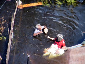 A Coast Guard rescue swimmer in Katrina’s floodwaters prepares an elderly man and woman for transport to safety. (U.S. Coast Guard)