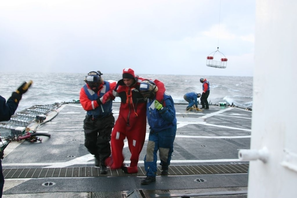 Alaska Ranger survivor in survival suit assisted from the rescue basket down to the improvised triage center in Munro’s galley. (Ensign Daniel Schrader, U.S. Coast Guard)