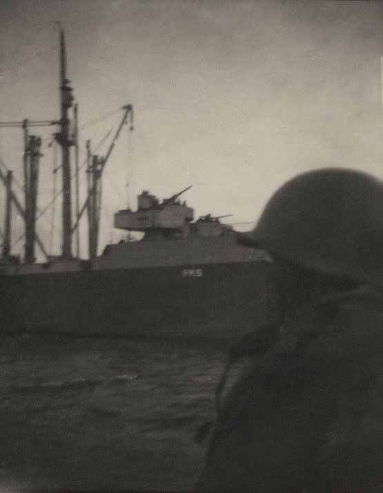 Faded image of a crewmember in a battle helmet looking on as CG-16 passes an attack transport on D-Day. (Courtesy of Hannigan family)