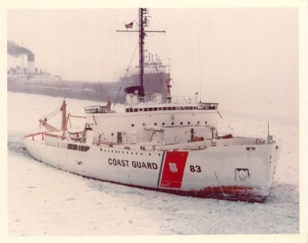 Coast Guard Cutter Mackinaw sporting the new “Racing Stripe” on its white hull escorting a Great Lakes bulk carrier through the ice. (U.S. Coast Guard) 