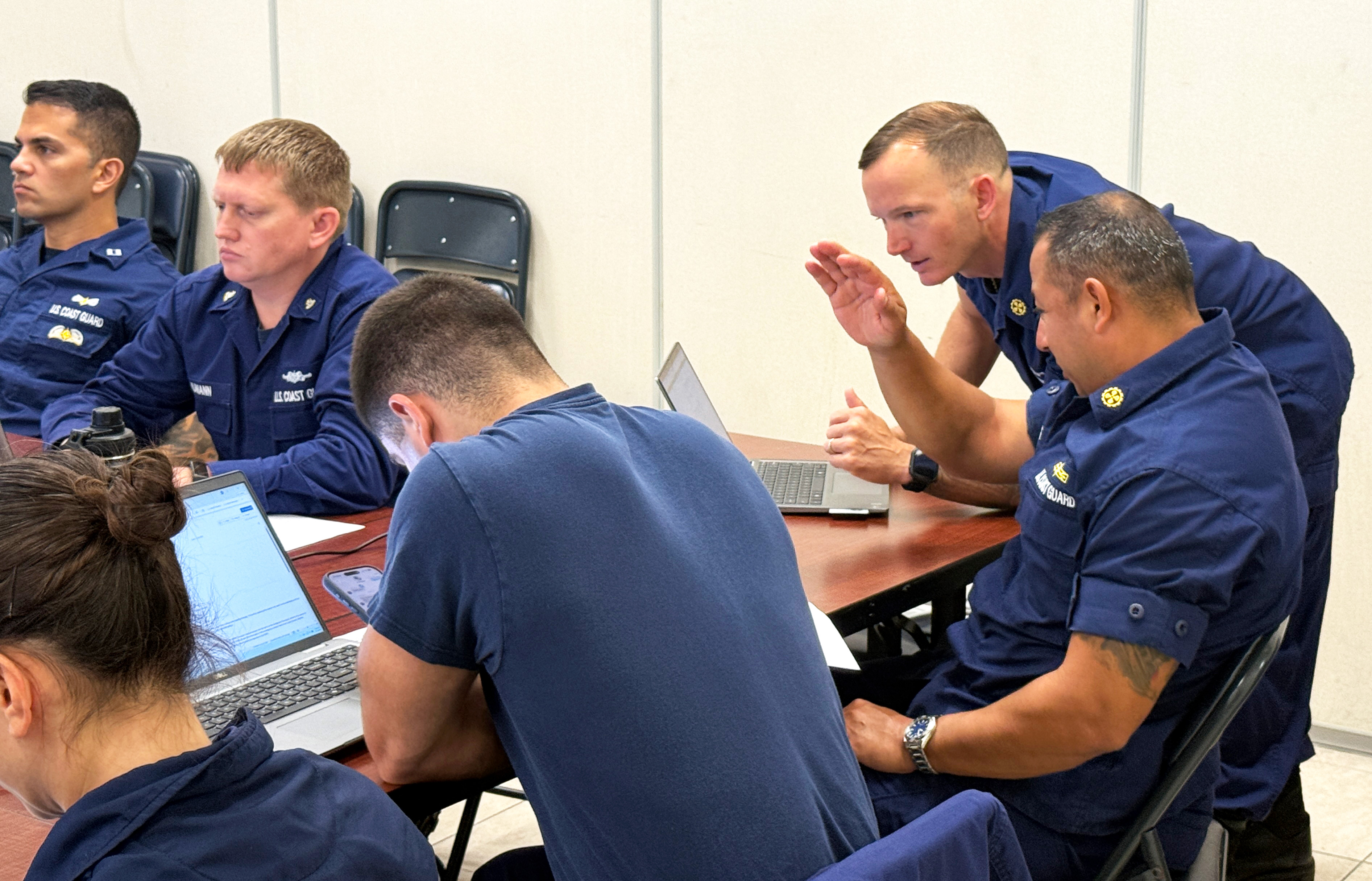 Chief Warrant Officer-2 Richard Picone (standing) reviews a draft email that Chief Warrant Officer-4 Timothy Buck (seated) created with the help of generative AI tools during AI training on June 2, 2026, in Miami. The warrant officers, both marine inspectors with Sector Miami, used what they learned in the workshop to find ways to streamline processes associated with their operational work.
